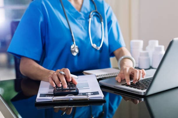 Biller working claims with a calculator, laptop, and stethoscope nearby
